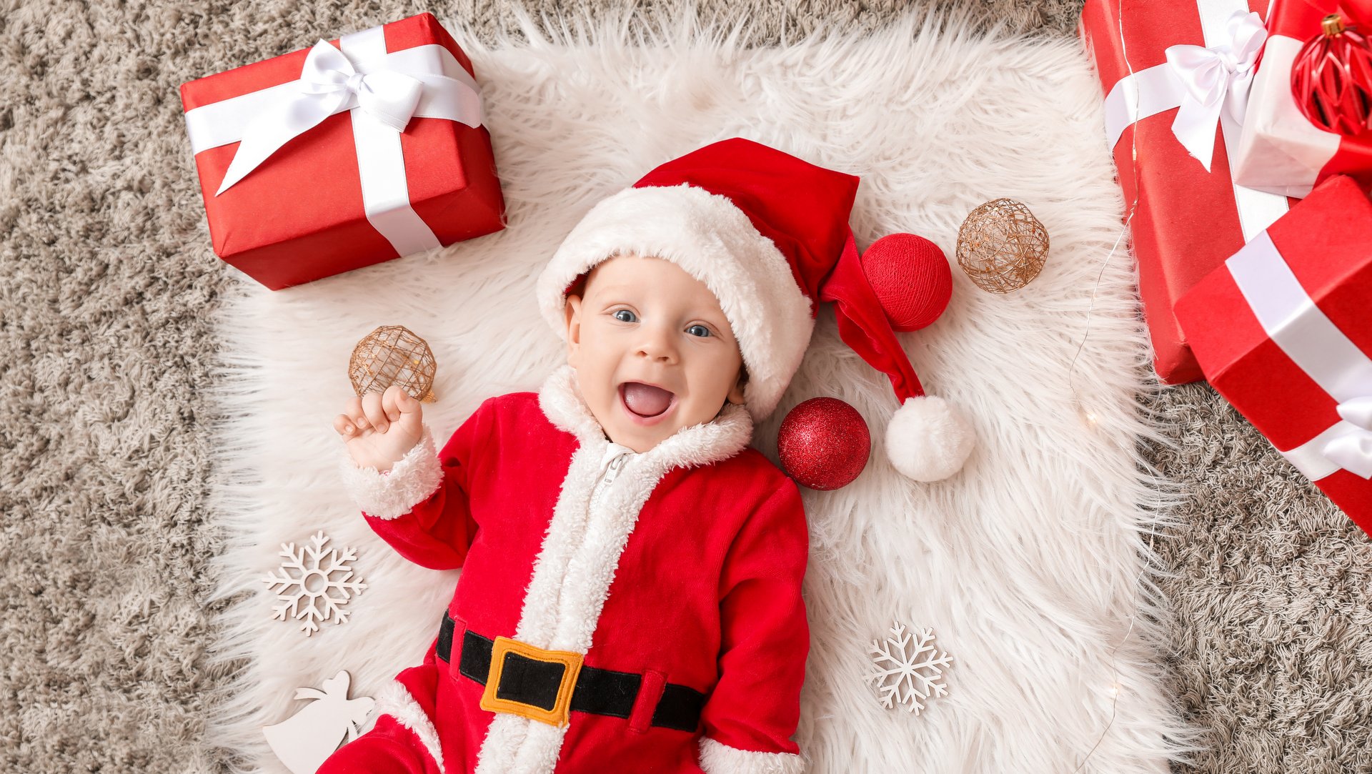 Cute little baby smiling in Santa Claus costume and with Christmas gift boxes