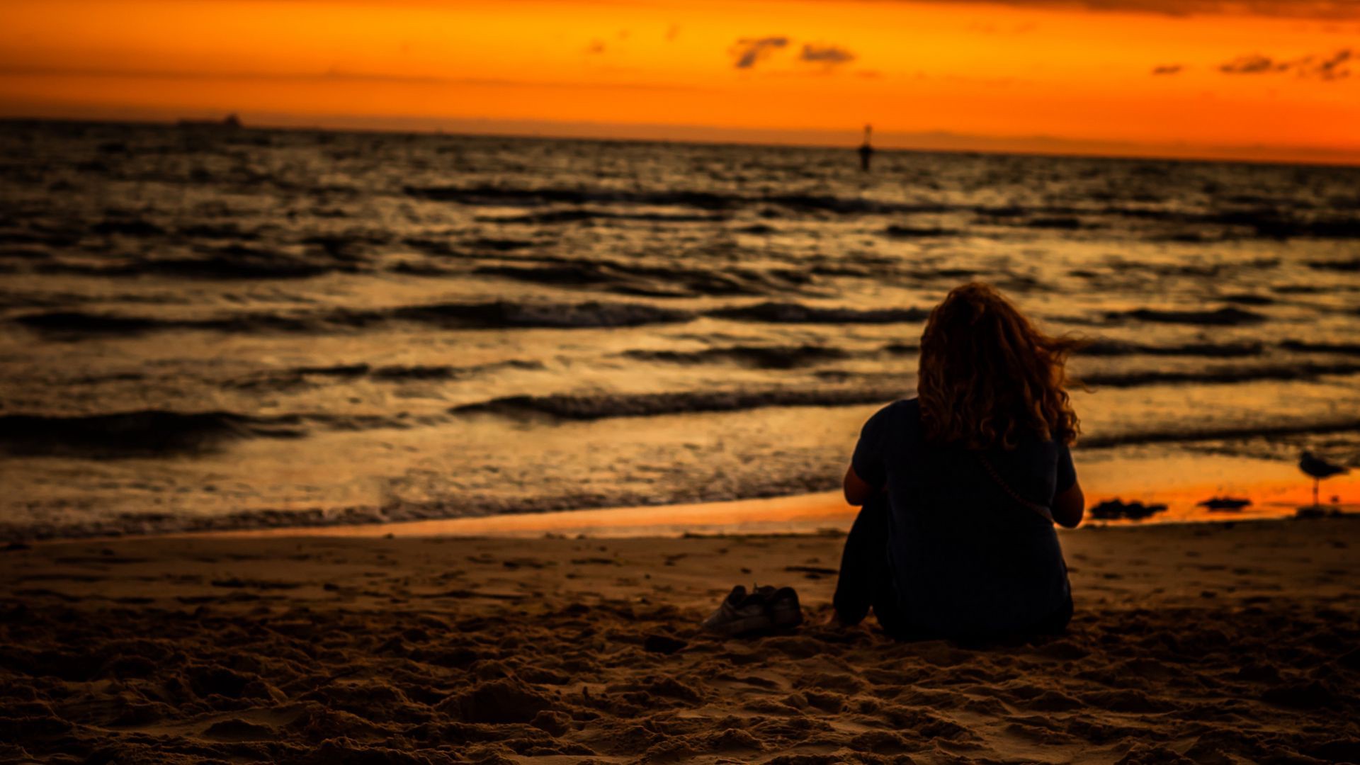 Girl Is Sitting On Beach Sand Watching Ocean Waves During Sunset 